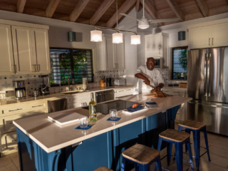 Chef preparing dinner in A Dream Come True Villa&rsquo;s kitchen with white cabinets and counters and a large central island.