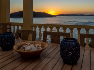 Outdoor dining table at A Dream Come True Villa on the Mahoe Bay waterfront with the ocean and sun setting in the background.
