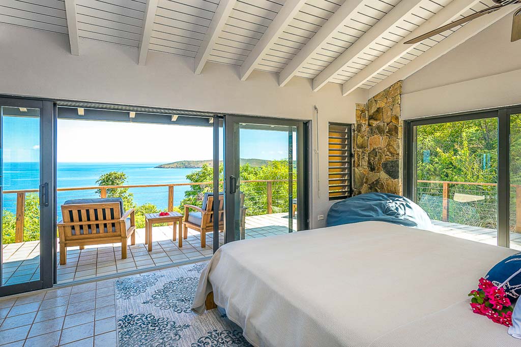 Alize Villa’s master bedroom with a king bed and large glass doors leading out to a porch with Leverick Bay in the background