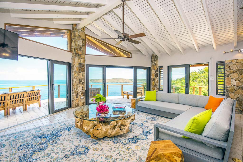 Alize Villa’s living area with an L-shaped couch, coffee table and flat-screen TV with a porch and the sea in the background.