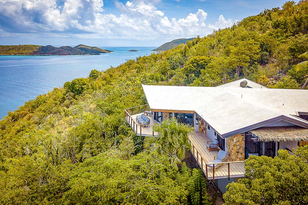 Alize Villa with a wrap-around porch on the hillside surrounded by tropical vegetation with Leverick Bay in the background.