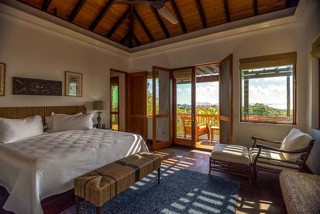 Guest room with a king bed, wood floor, lofted ceiling and a sitting area by glass doors leading to a private balcony.