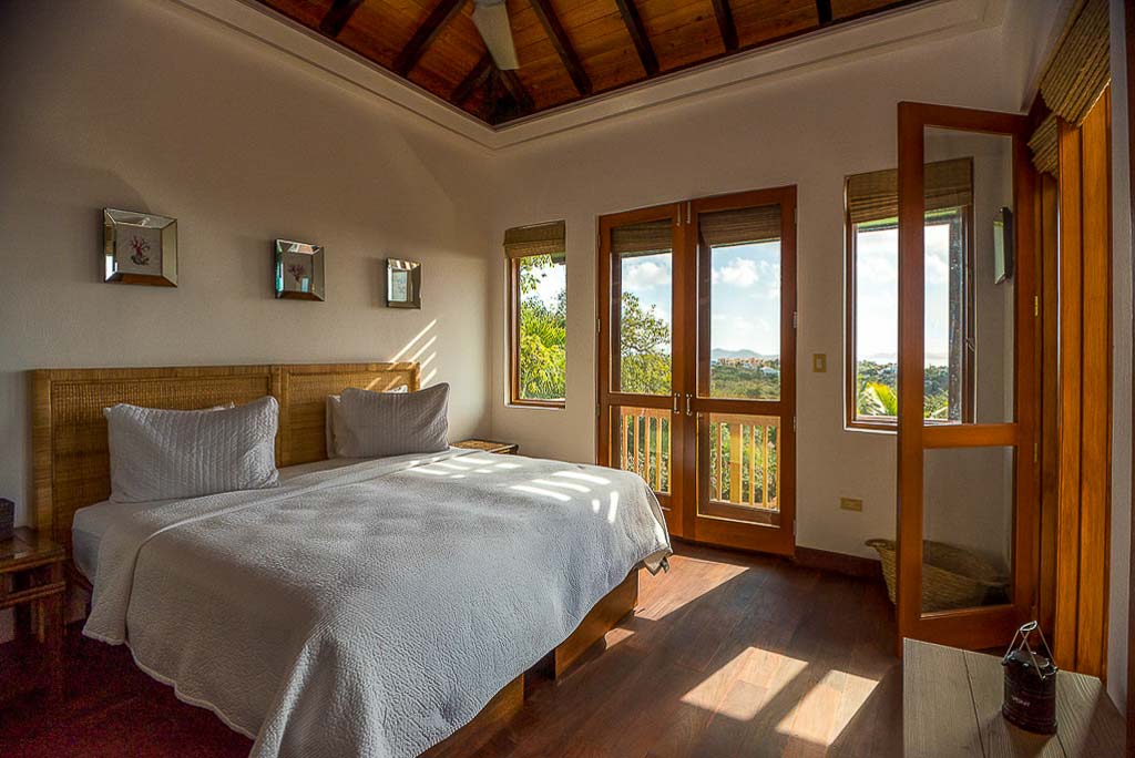 Twin bedroom at Amateras Villa with wood floors, natural hues and doors leading to a balcony looking out on the island.