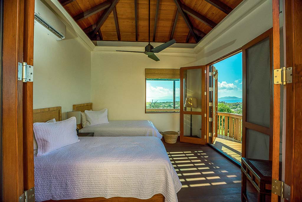 Guest room at Amateras Villa with two double beds, wood floors, a ceiling fan and open doors leading to a wooden deck.