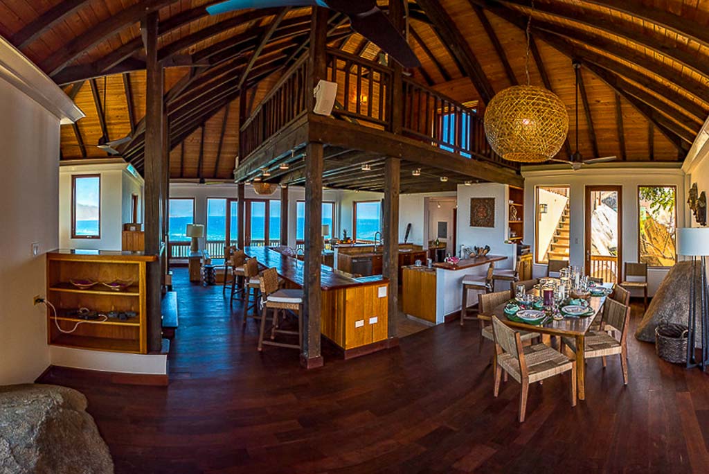 Amateras Villa’s main room with vaulted wood ceilings and a kitchen in the center surrounded by a bar next to a dining area.
