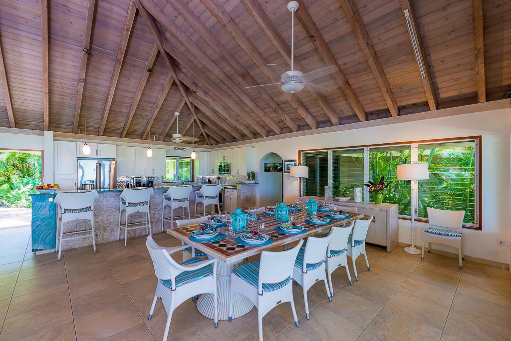 Bright and airy main room at Beachcomber Villa with a dining table set for 10 and a modern kitchen and bar in the background.