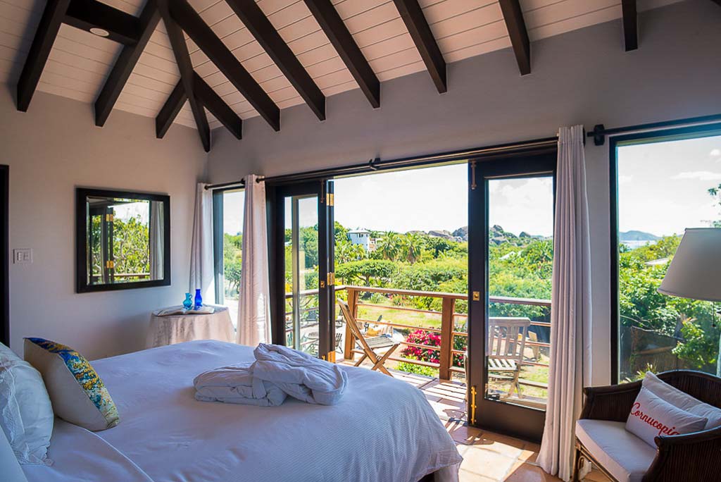 Cornucopia Villa guest bedroom with a king bed, lofted ceilings with dark wood beams and the door open to a private balcony.