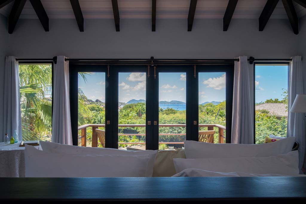 Guest bedroom with king bed and glass windows and doors to a private balcony with Little Trunk Bay in the distance.