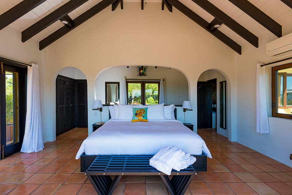 Superior suite at Cornucopia Villa with a king bed in the middle, tile floor, a lofted wood-bean ceiling and door to a patio.