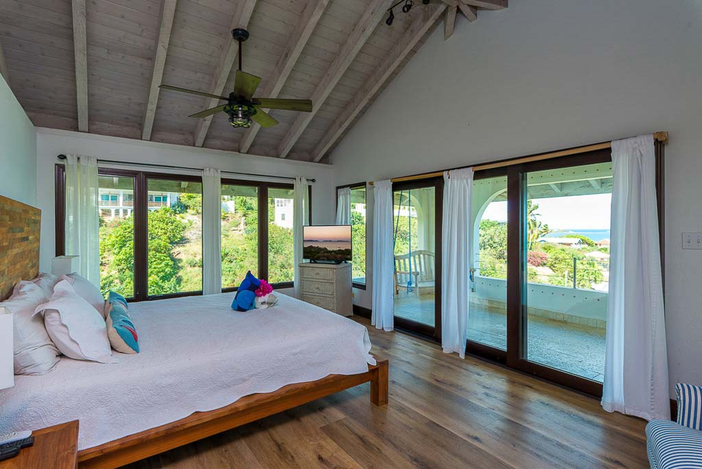 Dos Sols Villa’s master bedroom with a king bed on wood floors and a large private patio with an ocean view.