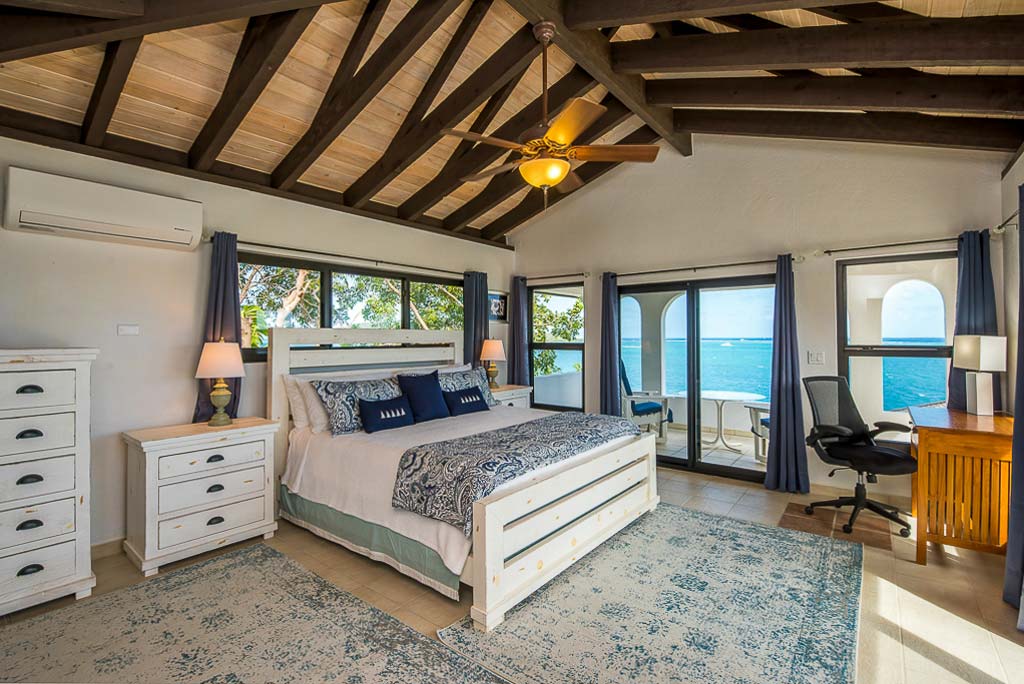 Master bedroom with a king bed, desk and chair and private patio area looking out on the blue waters of Leverick Bay.