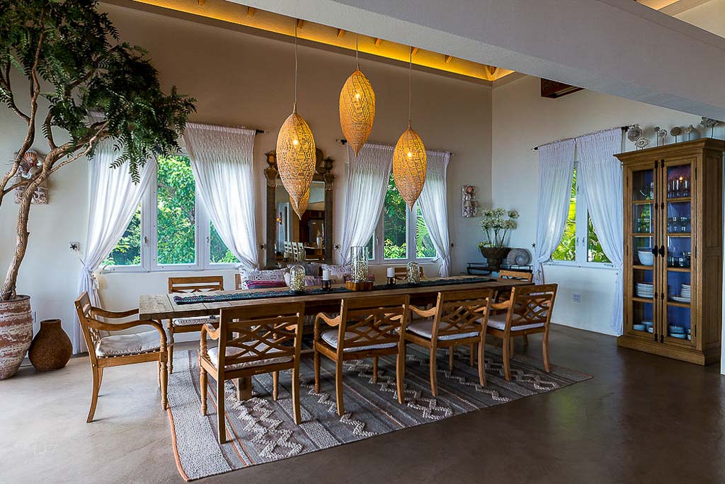 Formal dining area in La Vida Villa with modern hanging lights, smooth stone flooring and a cabinet containing tableware.