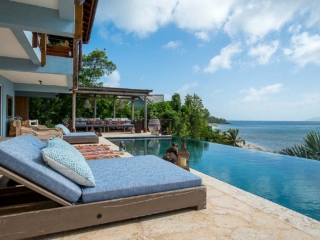 La Vida Villa: Pool Stone patio with cushioned lounge chairs next to a pool with an outdoor dining area and Nail Bay beach in the background.