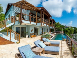 La Vida Villa: Poolside Porch A natural stone patio with lounges and a pool in front of La Vida Villa with multiple glass doors and second level balconies.