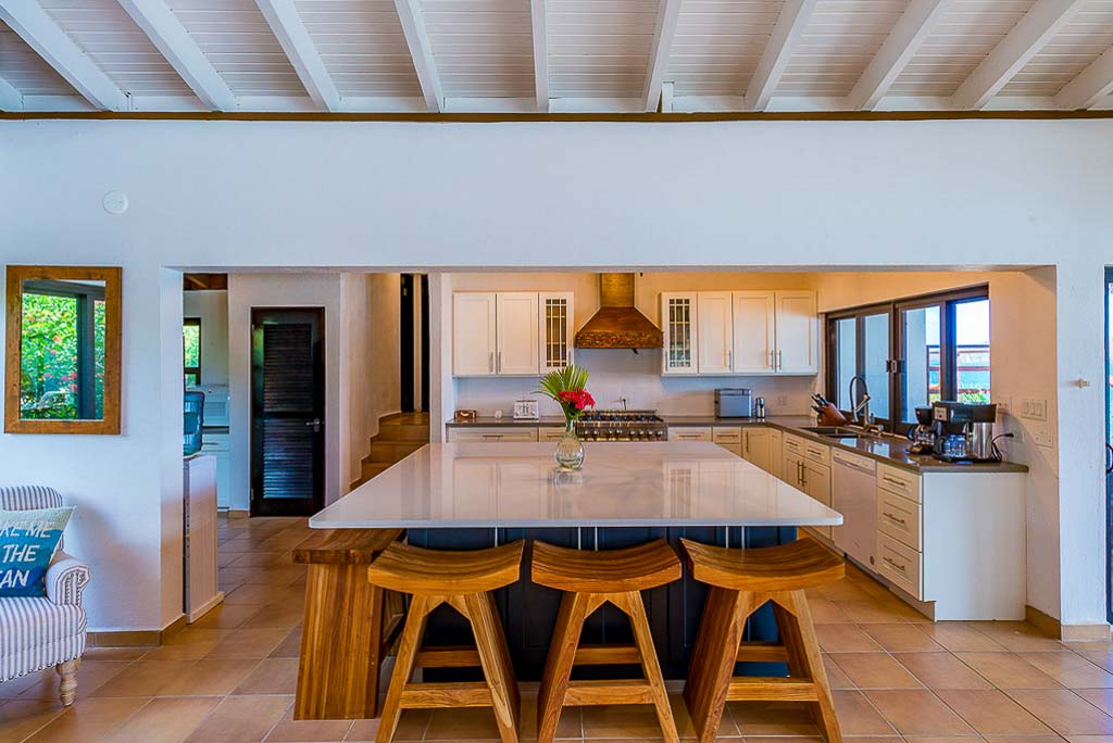 Modern, open kitchen at Rainbow’s End Villa with a large granite-top island and comfortable wooden stools to sit and dine.