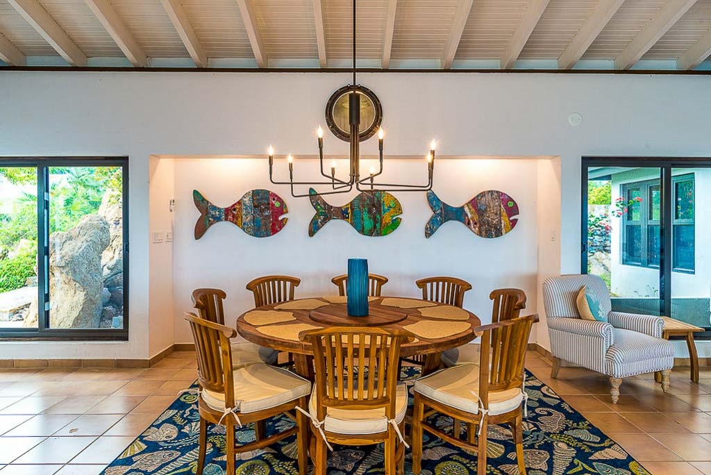 Circular dining table at Rainbow’s End Villa with a chandelier above and large windows on either side letting in natural light.