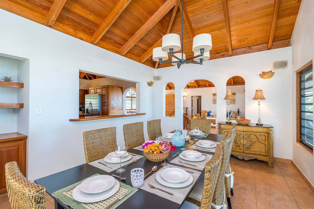 Sea Palms Villa’s formal dining room with a large retangular table, white walls, a chandelier and lofted wood-beam ceilings.