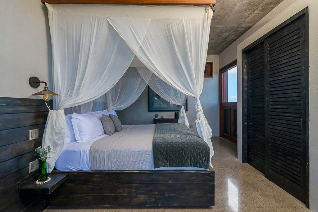 Segura Villa master bedroom with a king bed and décor of dark wood accents and muted and natural hues.