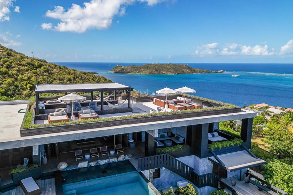 Segura Villa facade and outdoor space with a luxurious rooftop sundeck on a lush hill overlooking Leverick Bay on a sunny day.
