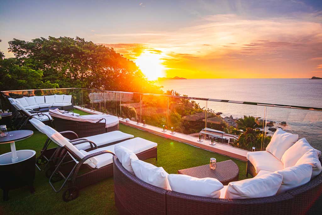 Turf-covered sun deck at 1 Paradise Lane Villa with white-cushioned patio furniture looking out on a sunset on Nail Bay.