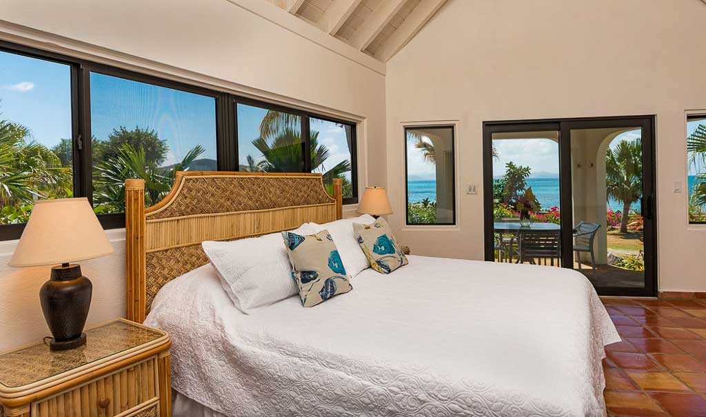 Beach Dream king bedroom with windows along the wall and a sliding glass door leading to an ocean-side patio on Mahoe Bay.