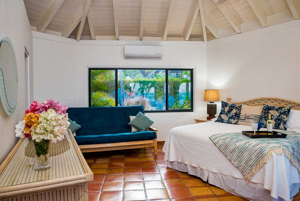 Beach Dreams Villa guest room with king bed, tile floor and couch by a window looking out on a tropical garden.