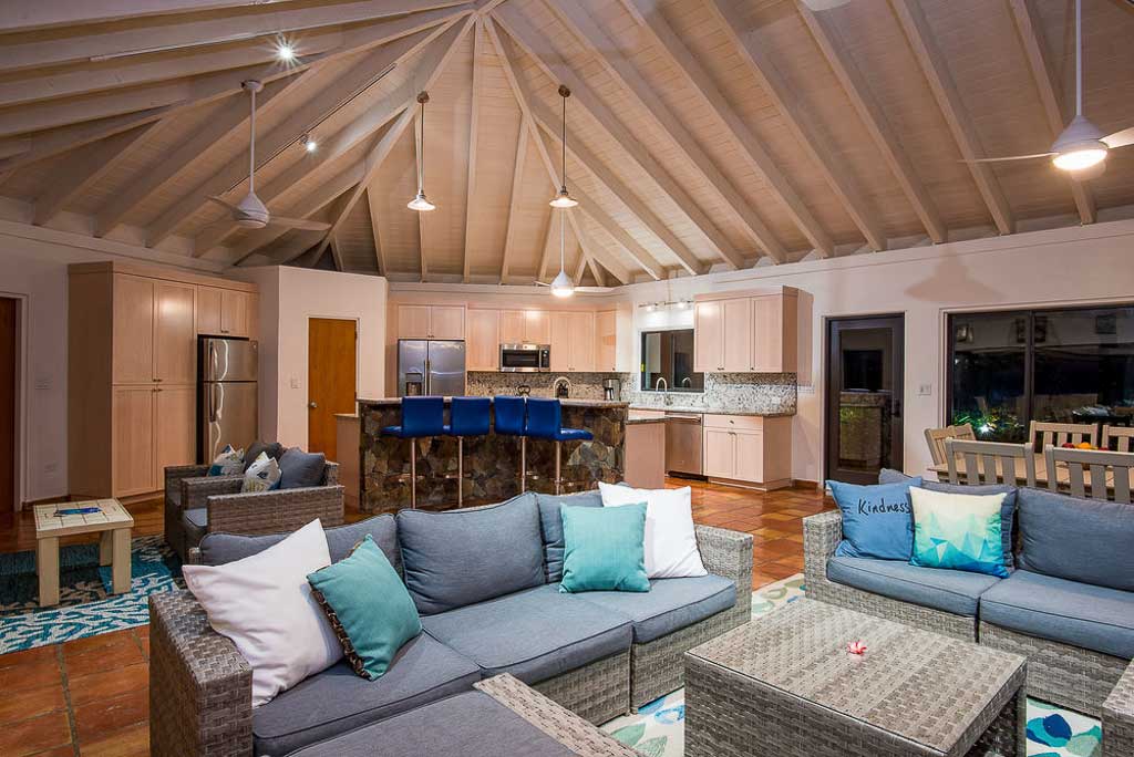 Open main room at Beach Dreams Villa with vaulted, wood-beam ceilings, comfortable living area and kitchen in the background.