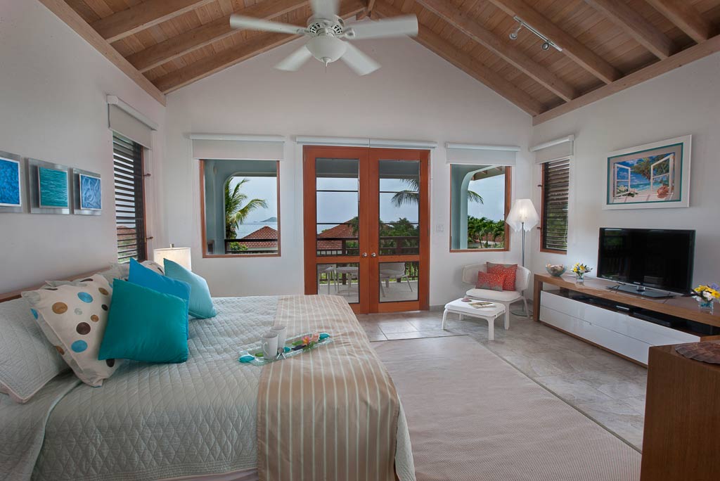 Blue Lagoon Villa’s master bedroom with a king bed, sitting area, flat screen TV and glass doors leading to a private patio.
