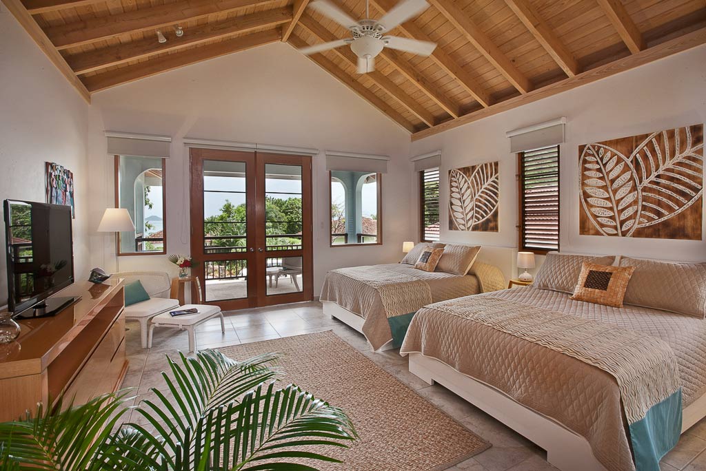 Blue Lagoon Villa guest room with two queen beds, light, natural decor and double glass doors leading to a private patio.
