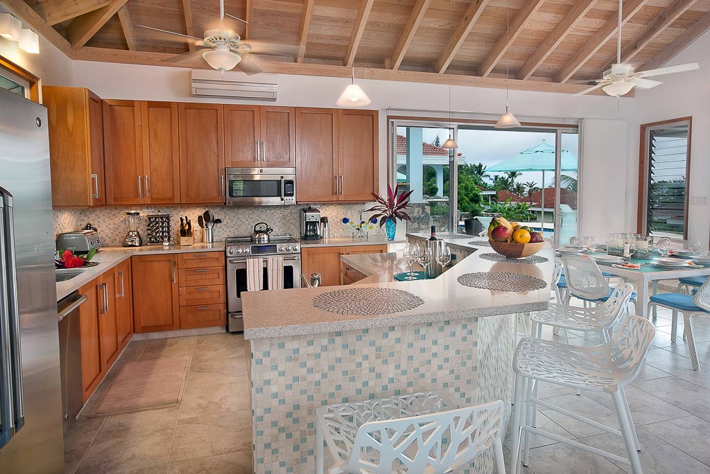 Blue Lagoon Villa’s large modern kitchen with a bar-style island, light counter tops, steel appliances and ceiling fans.