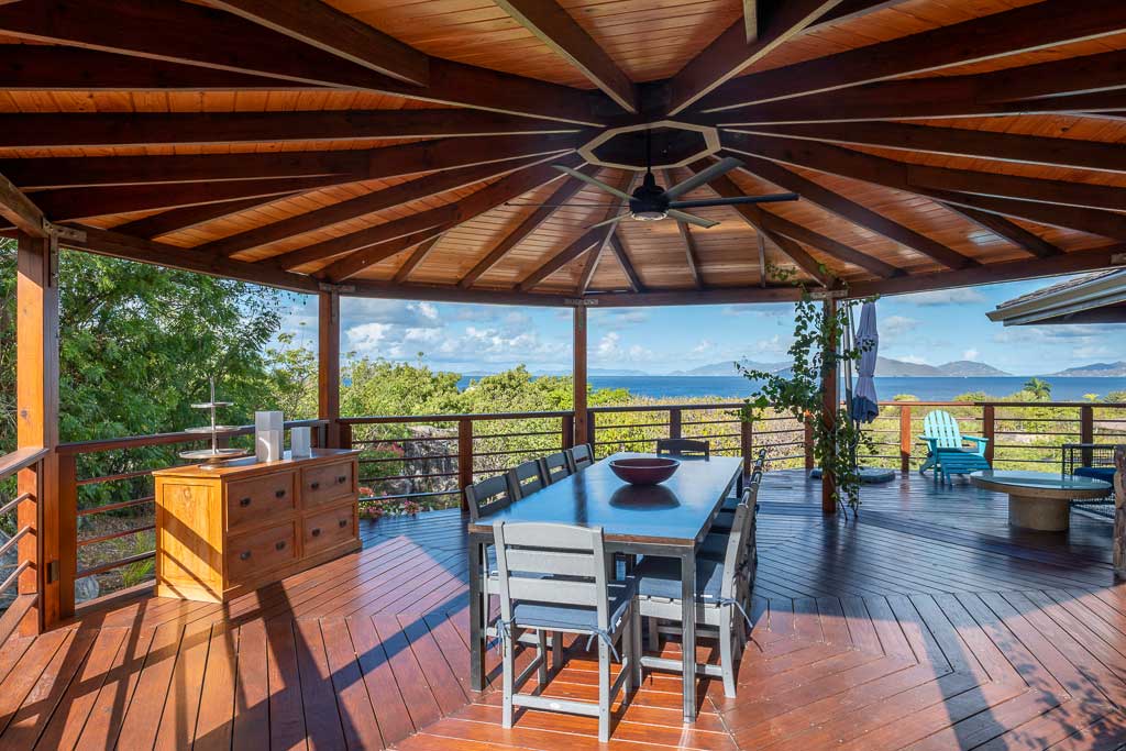 Outdoor dining area on the wooden covered deck of Eden Waters Villa with Little Trunk Bay in the background.