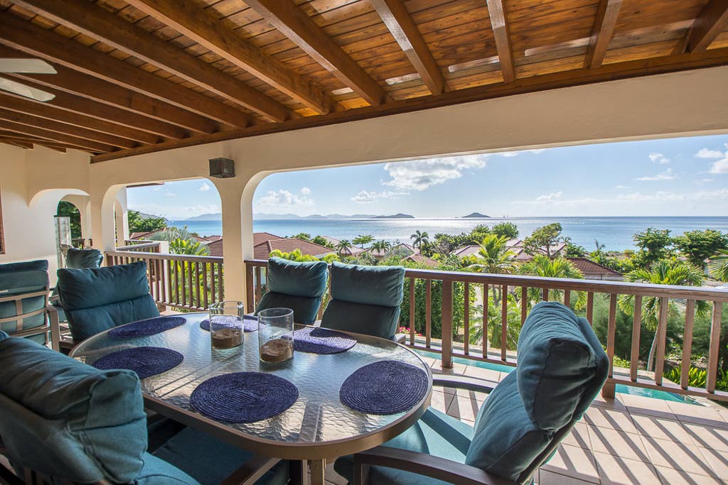 Loblolly Villa’s outdoor dining area on a covered porch with the sun shining on Mahoe Bay in the background.