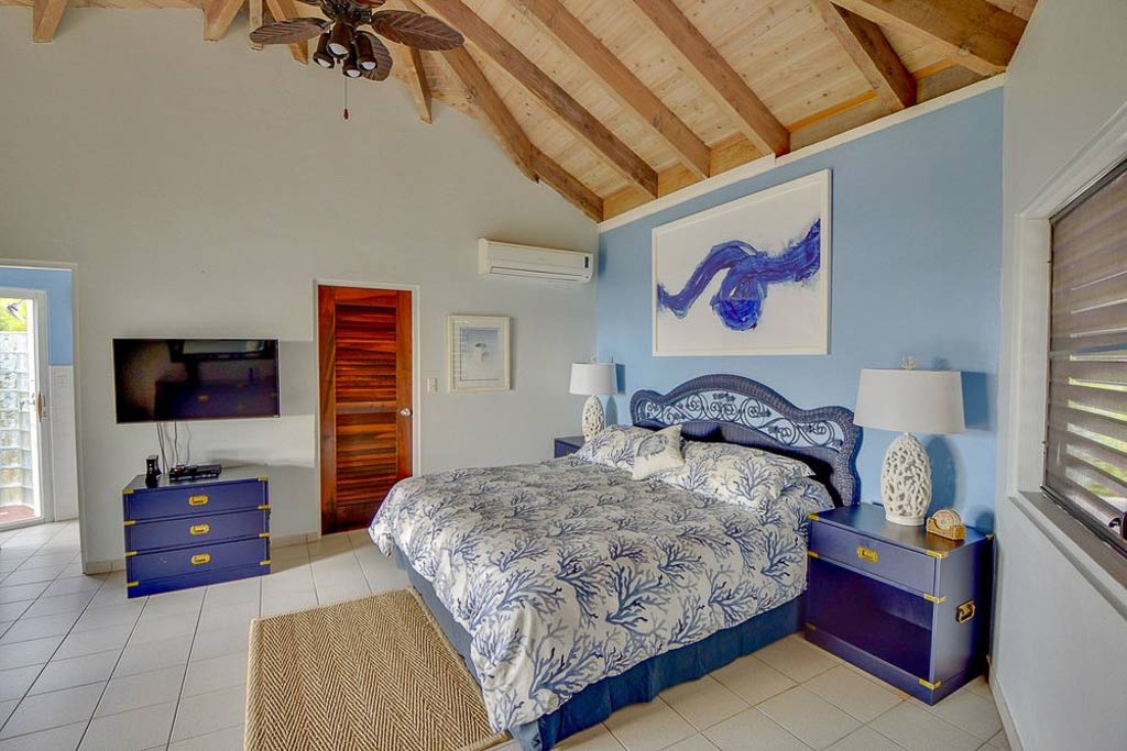 Sandcastle Villa guest room with king bed, bed-side tables, white tile floors and a flat-screen TV mounted on the wall.