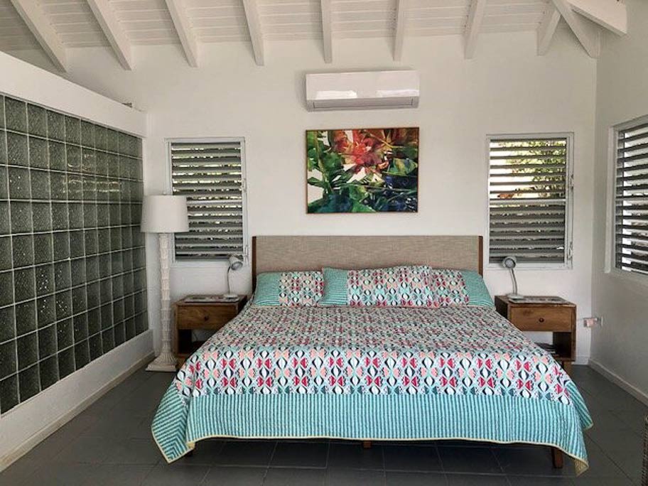 Bedroom area of Sea Breeze Villa with a king bed, wooden bed-side tables with lamps and multiple windows.