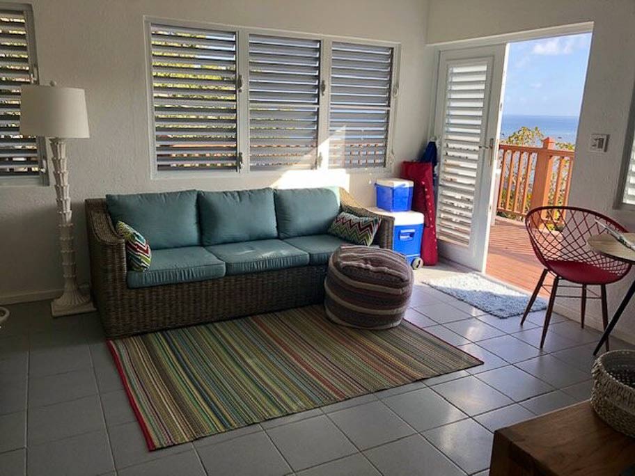 Entrance to the Sea Breeze Villa main room with a wicker couch and windows with wooden blinds looking out on Leverick Bay.
