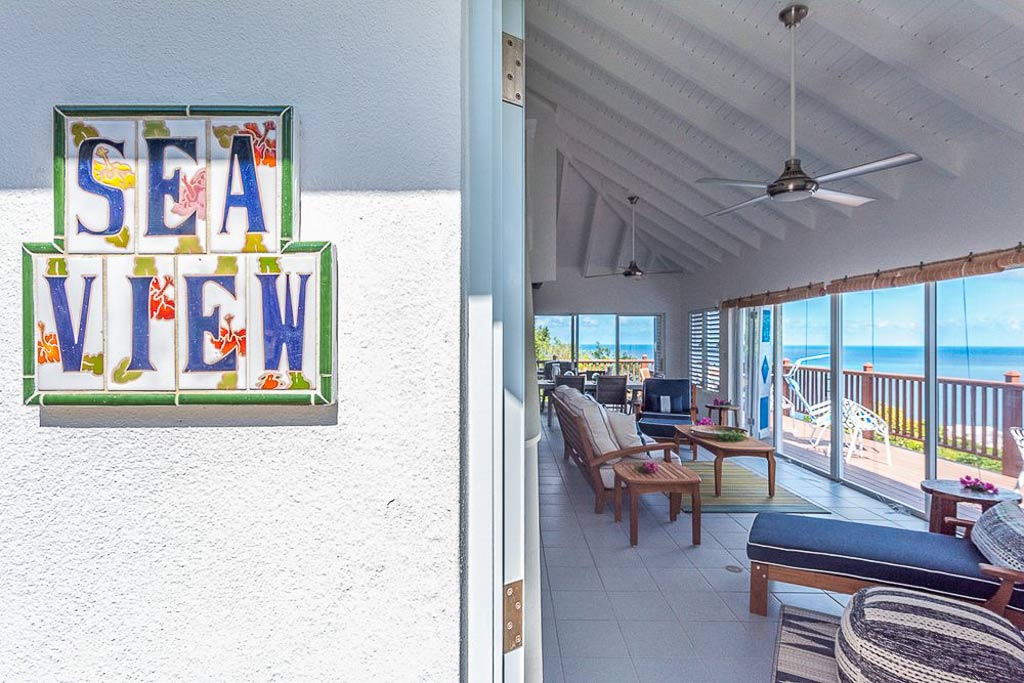 Tile sign reading Sea View on the villa wall next to a door open to the main room living and dining areas.