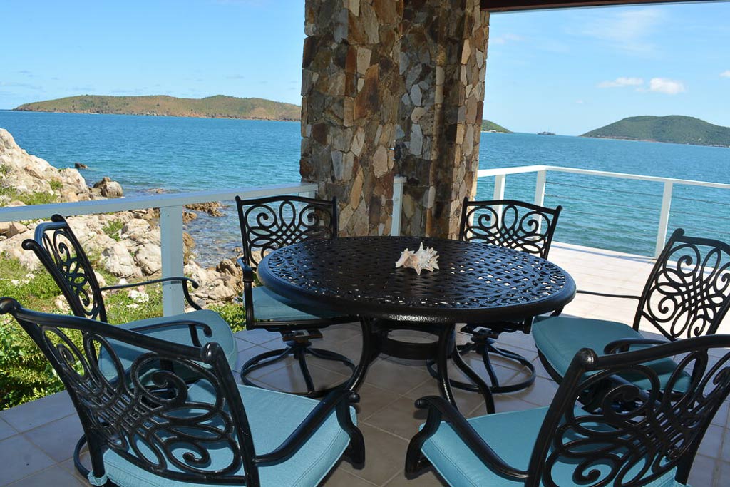 Outdoor dining area on Serendipity Villa’s patio with the rocky shore and the blue waters of Leverick Bay in the background.