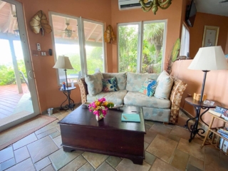 Living room at Sundowner Villa with stone tile floors, a couch and coffee table with large windows and a door to the patio.