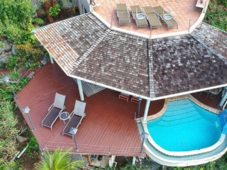 Plunge pool and patio at Sundowner villa with a rooftop sun deck with lounge chairs above surrounded by tropical vegetation.