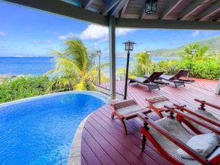 Red wood deck with lounge chairs poolside facing out to beautiful Nail Bay on a bright and sunny day.