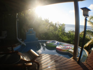Covered wood sundeck next to a plunge pool boarded by green trees and shrubs beachside at Nail Bay, Virgin Gorda.