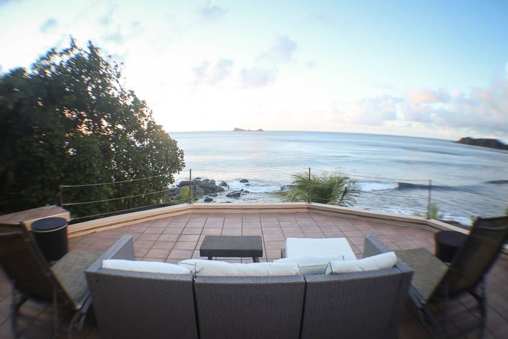 Sunset Watch Villa’s oceanfront natural-stone patio with couch and lounge chairs looking out at the beach and Nail Bay.