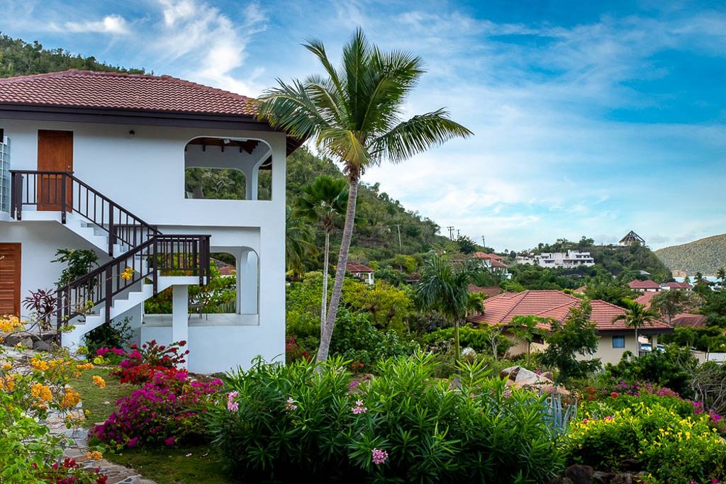 Two-level Villa ValMarc pavilion on the hillside at Mahoe Bay surrounded by palm trees, flowers and lush tropical vegetation.