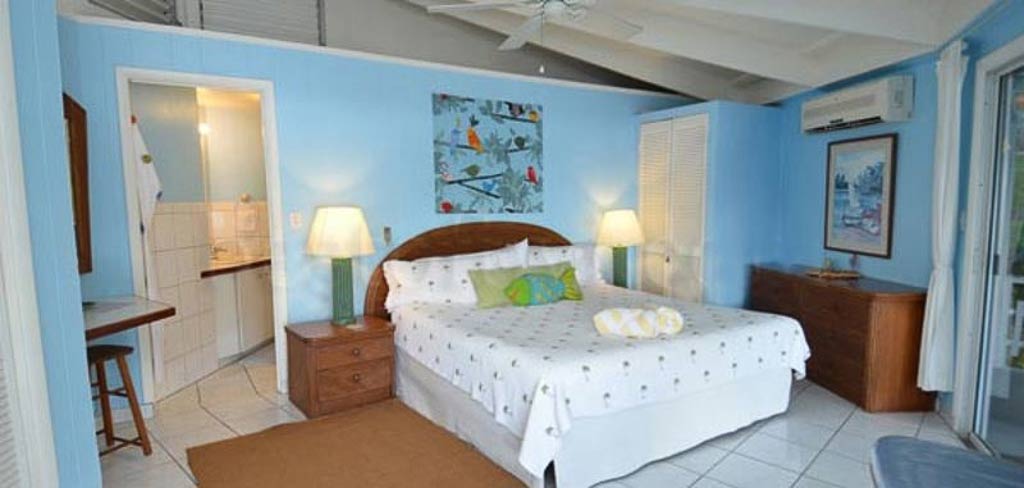 Guest bedroom at Vista Villa with a king bed, bright island-style décor, lofted ceiling and door open to the en-suite bath.