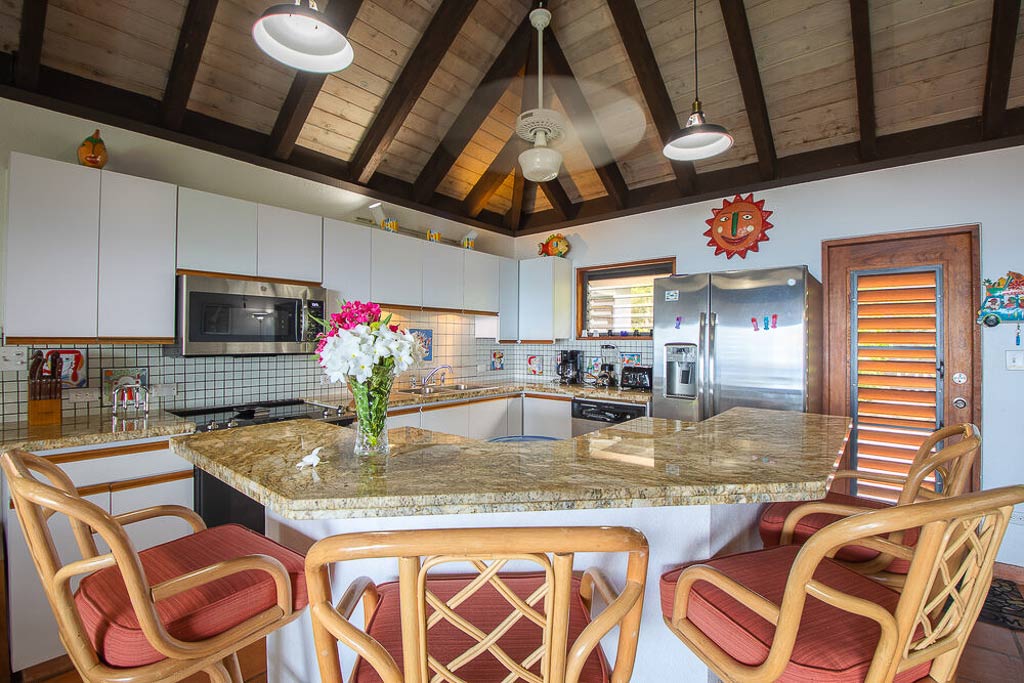 Open kitchen at Villa Del Sole with white cabinets, steel appliances, granite counters and an island with high-back stools.