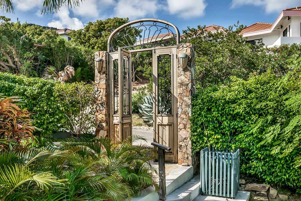 Purpleheart wood and iron gate at Coconut Grove Villa leading to a natural stone path surrounded by tropical gardens.