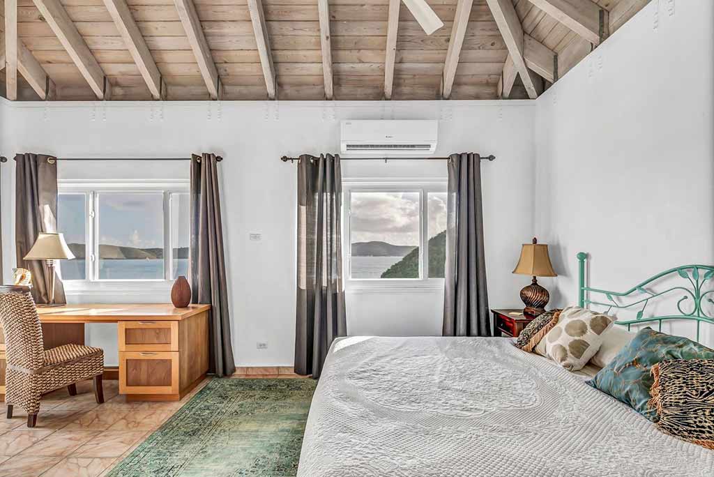 Coconut Grove villa’s master bedroom with king bed, deck and chair and windows looking out on Leverick Bay.