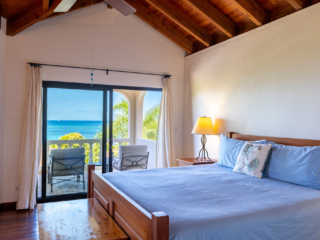 Bellamare Villa: Bedroom Guest room with a king bed and side table with a lamp next to a glass door to a patio with Mahoe Bay in the background.