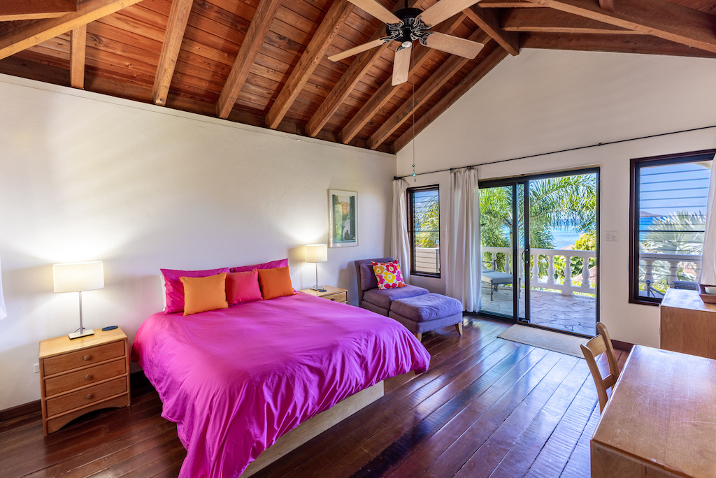 Bellamare Villa bedroom with king bed, white walls, natural wood floors, vaulted ceilings and a door leading to a stone patio.