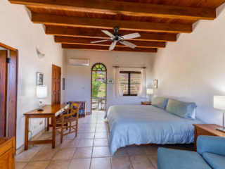 Bellamare Villa: Bedroom Guest room at Bellamare Villa with a king bed, desk with chair, tile floor, a wood-beam ceiling and open door to a patio.